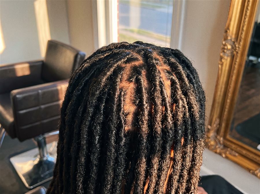 A close crop of neatly retwisted dreadlocks catching warm salon light