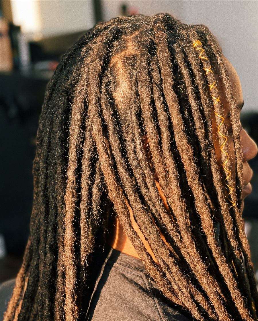 A side profile close crop of long finished dreadlocks with a fine gold thread wrap near the root